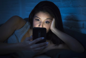 young beautiful womanl in bed using mobile phone late at night at dark bedroom lying happy and relaxed enjoying social media network at her phone in communication