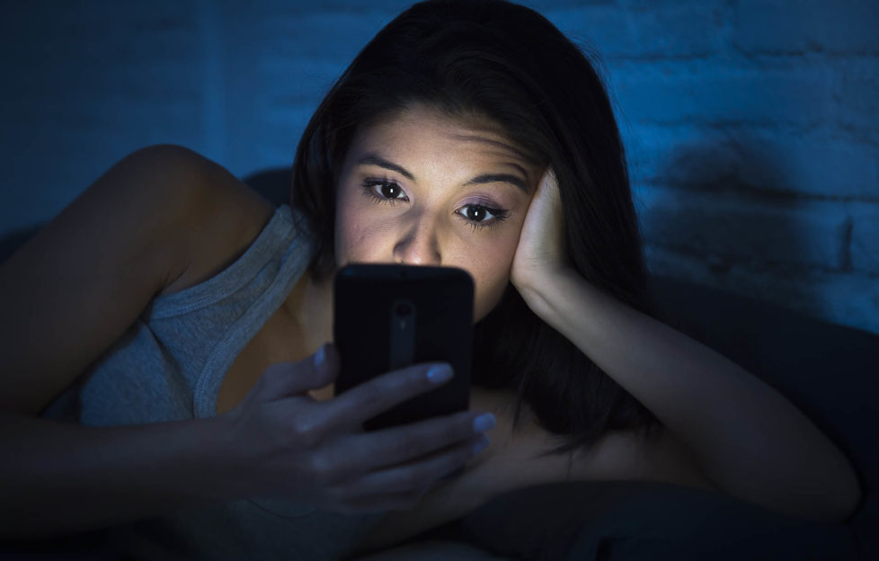 young beautiful womanl in bed using mobile phone late at night at dark bedroom lying happy and relaxed enjoying social media network at her phone in communication