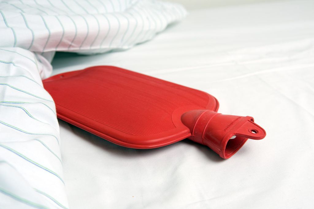 Red hot water bottle on white sheets in bed