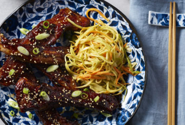Deep reddish well cooked spare ribs with shredded cabbage and carrot on blue plate, chopsticks on the side