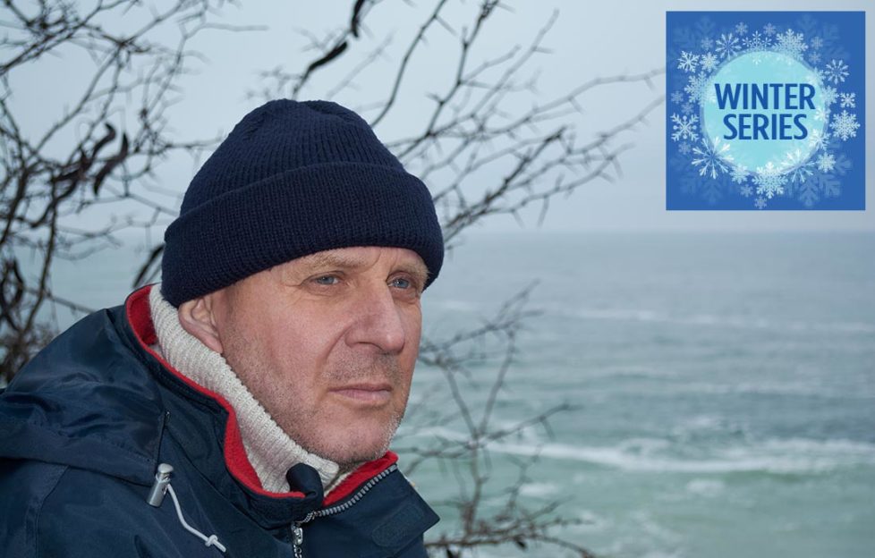 Pensive mature man in hat and coat looks out over the sea