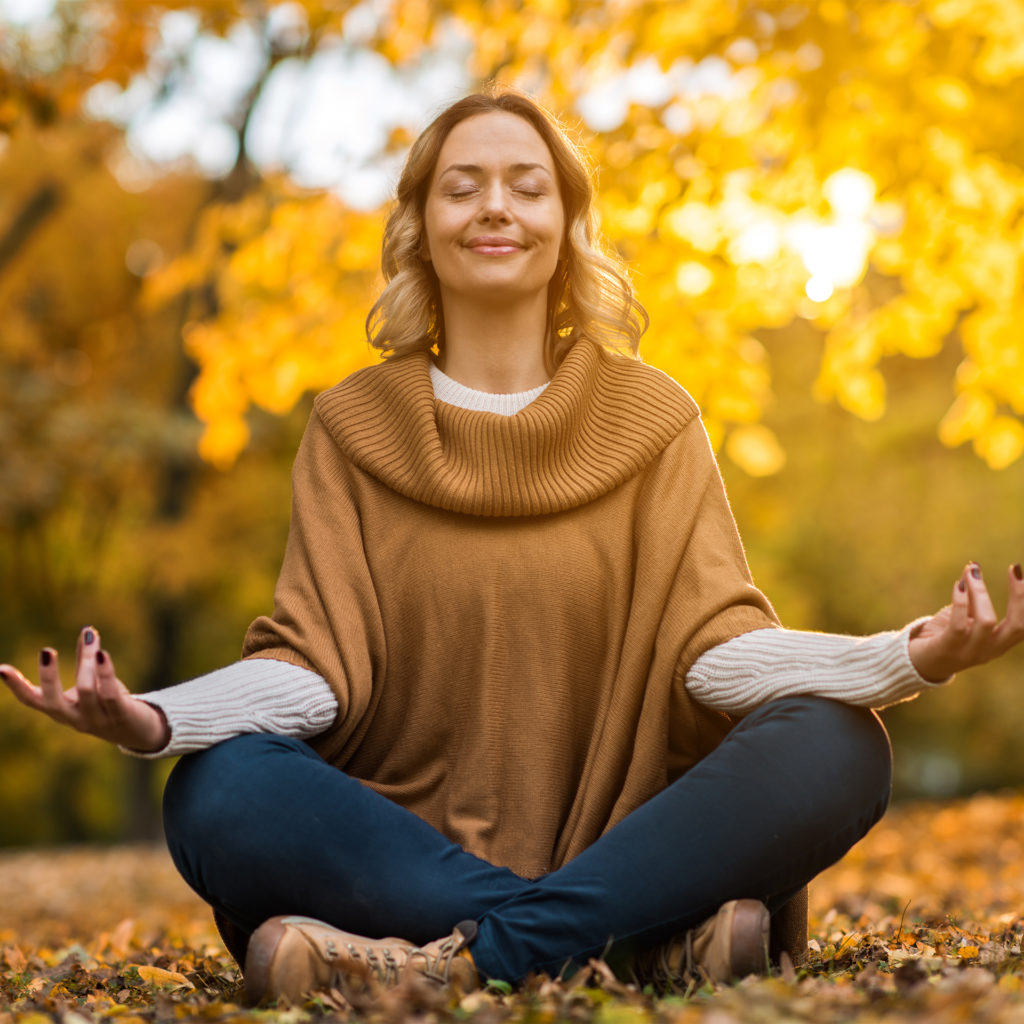 Woman sitting cross legged in wood in autumn, yoga pose