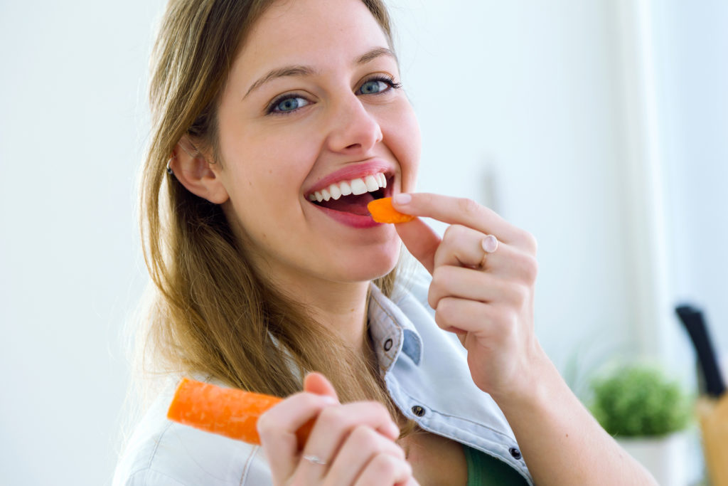 Portrait of pretty young woman eating carrot in the kitchen.