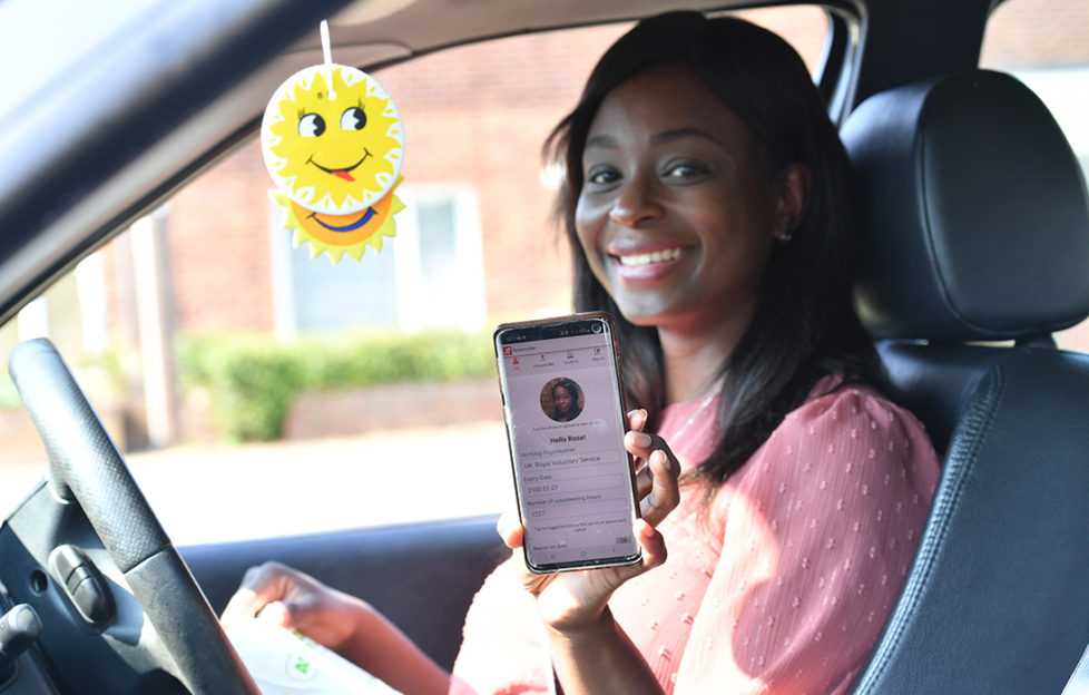 Smiling woman in car holds up phone showing NHS responder app