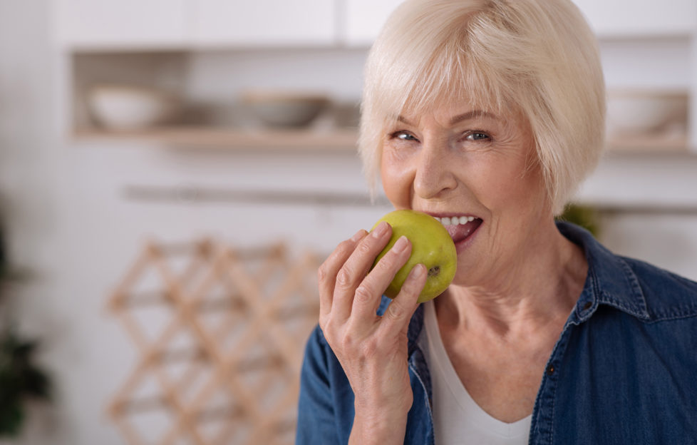 Older woman eating an apple in her kitchen