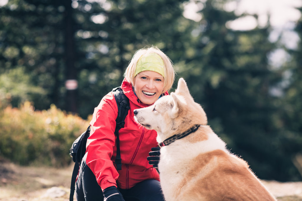Woman hiking with akita inu dog on forest trail. Friendship, recreation and healthy lifestyle outdoors, autumn woods in mountains, inspirational nature. Fitness and trekking and activity concept.; 