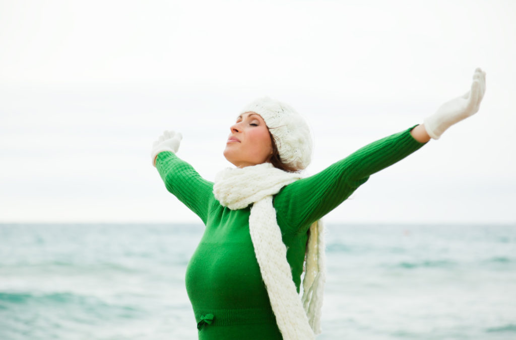 Woman in green top and white wooly hat standing on beach