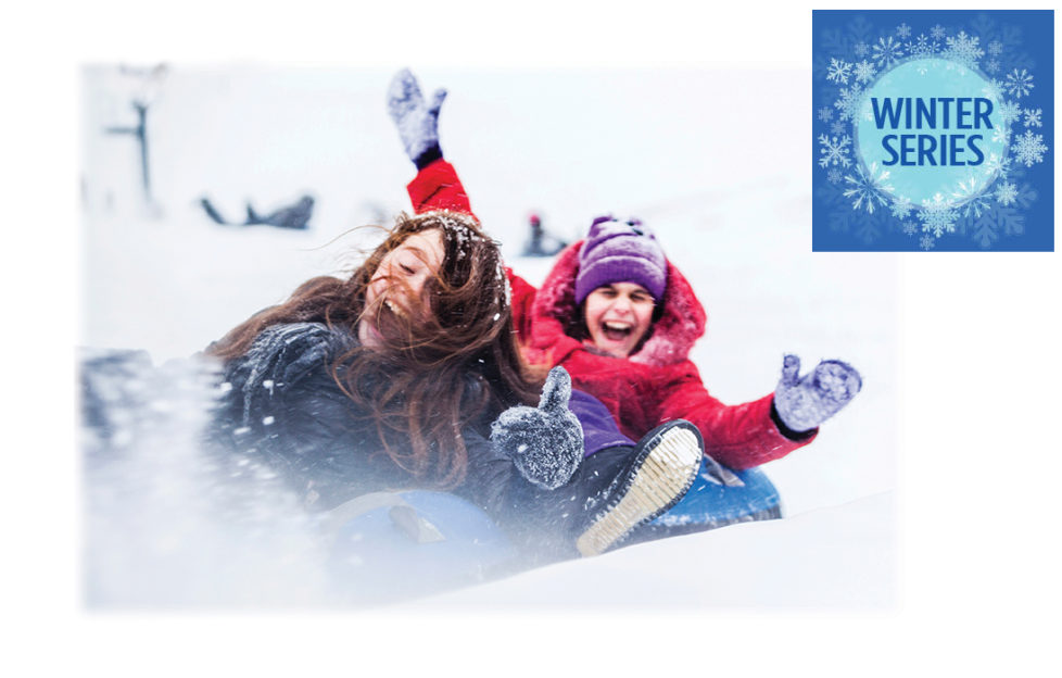 2 teenage girls sledging down a hill laughing, one in red, one in blue
