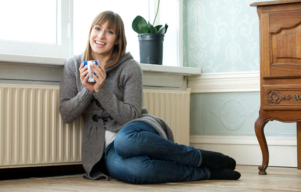 Woman with mug sits by radiator