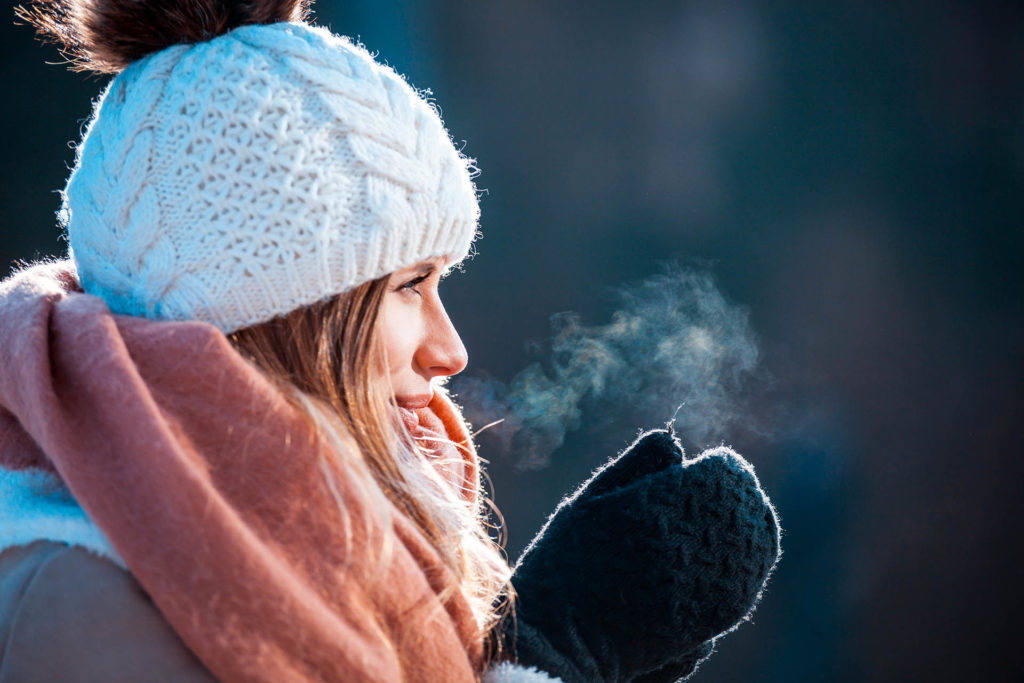 Woman breathing on her hands to keep them warm at cold winter day; 