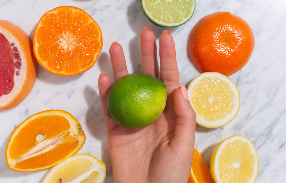 Hand with lime in it, surrounded by grapefruit, oranges and lemons.