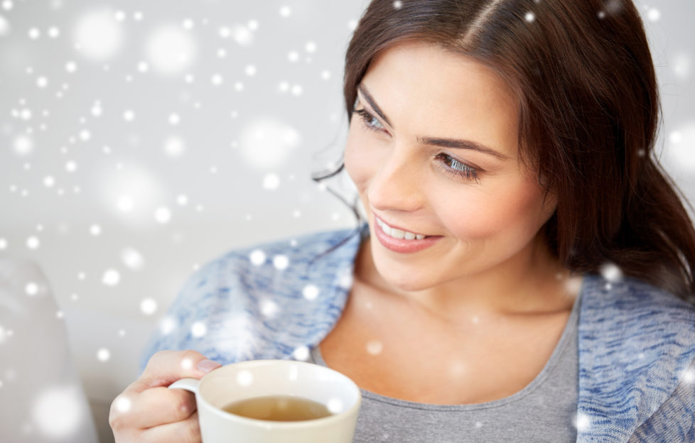 people, drinks, christmas and winter concept - happy young woman with cup of tea at home over snow;