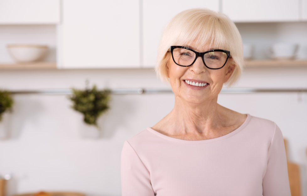 Enjoy home atmosphere. Nice cheerful aged woman smiling and standing in the kitchen;