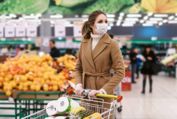 Shopping during the coronavirus Covid-19 pandemic. A young woman buys food in a supermarket with shopping cart. Woman in facial mask and gloves to prevent infection.;