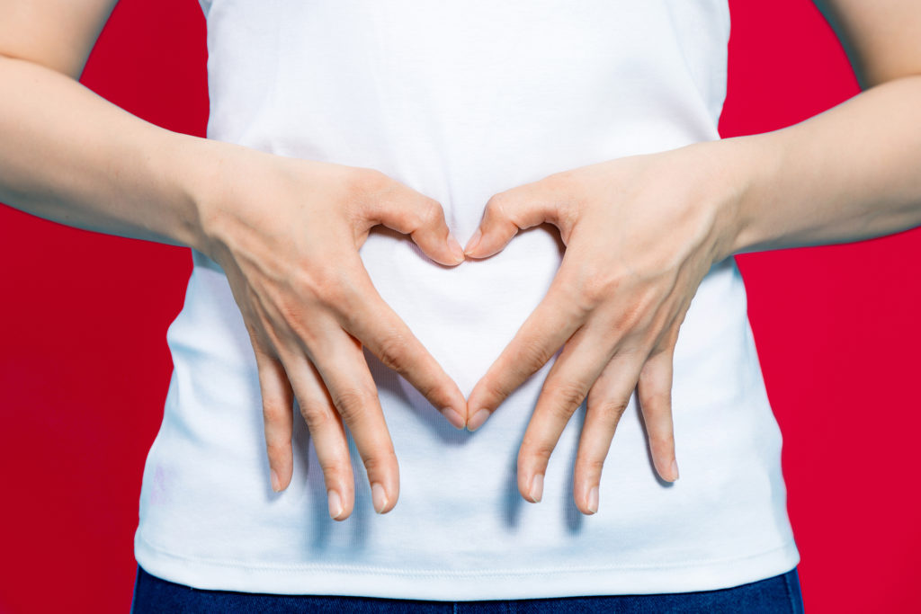 young woman who makes a heart shape by hands on her stomach.; 