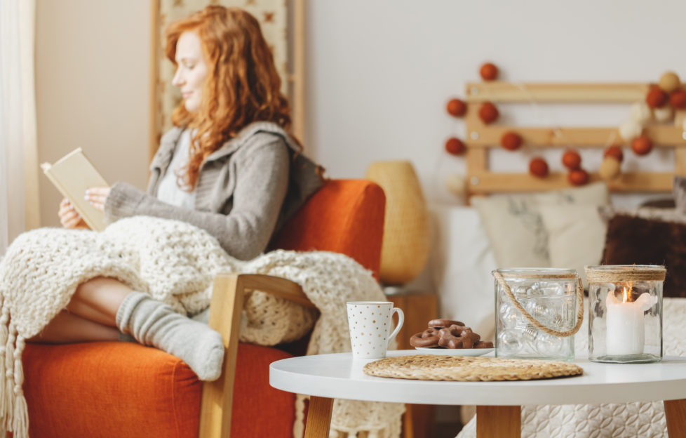 Small table with gingerbread and a tea along with a candle and a young lady reading a book in the background