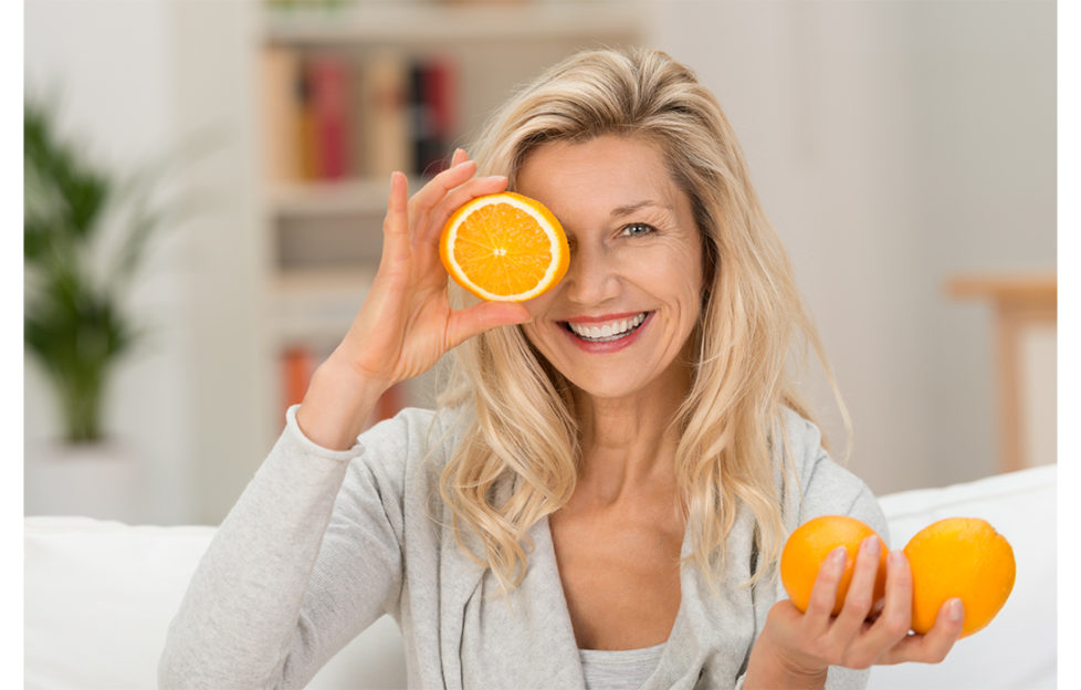 Woman holding up half an orange to the side of her face