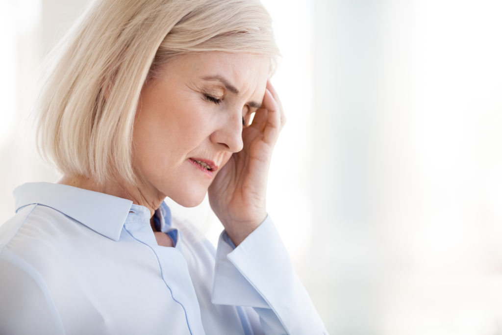 Tired upset mature old businesswoman suffering from strong chronic headache migraine or memory loss at work, stressed dizzy fatigued middle aged senior woman office worker feels pain in aching head; 