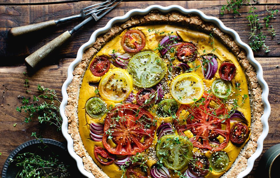 vegan quiche made with tofu and hazelnuts, topped with different coloured tomatoes and thyme sprigs