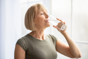 Fit senior woman drinking clear water during her workout break at home. Mature Caucasian lady staying hydrated after sports training. Healthy lifestyle and wellness concept;