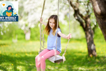 Cute little girl having fun on a swing in blossoming old apple tree garden outdoors on sunny spring day.