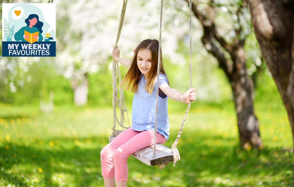 Cute little girl having fun on a swing in blossoming old apple tree garden outdoors on sunny spring day.