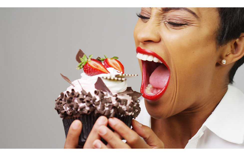 Black woman taking a huge bite out of a fancy dessert;