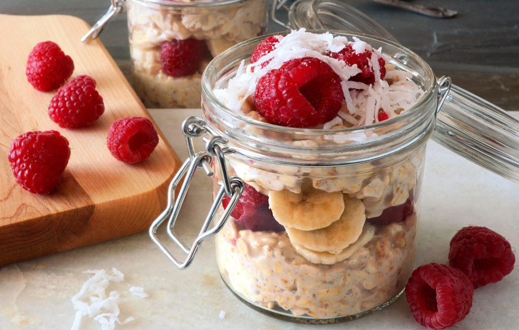 Healthy breakfast overnight oats with fresh raspberries and shredded coconut in a glass jar; 