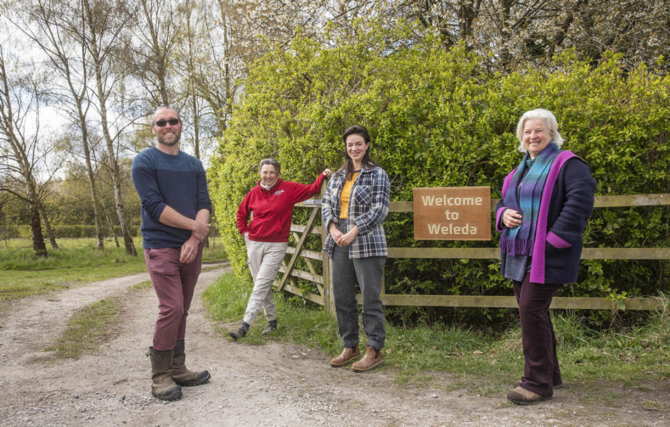 4 people standing by farm gate, wooden Weleda Garden sign