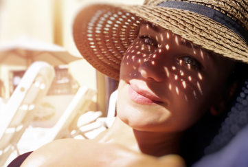 Pretty woman on the beach, closeup portrait of a nice female hides her face from the sun under a straw hat, skin protection, happy healthy summer vacation