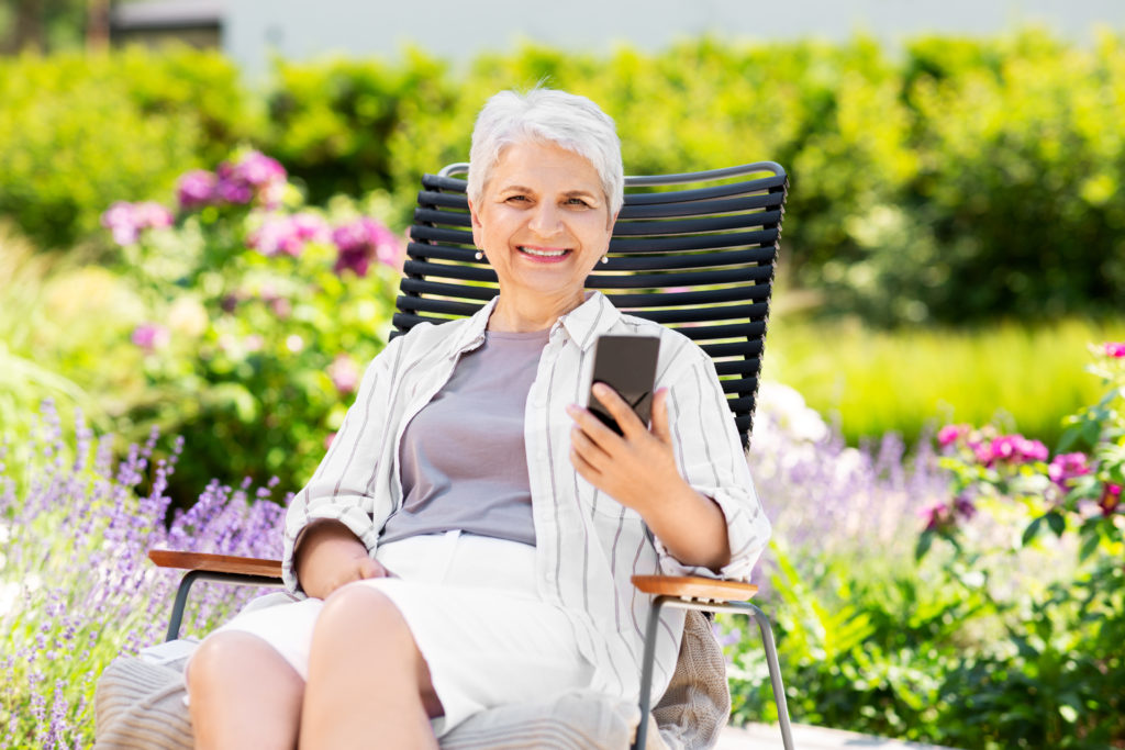 technology, old age and people concept - happy smiling senior woman with smartphone resting at summer garden; 