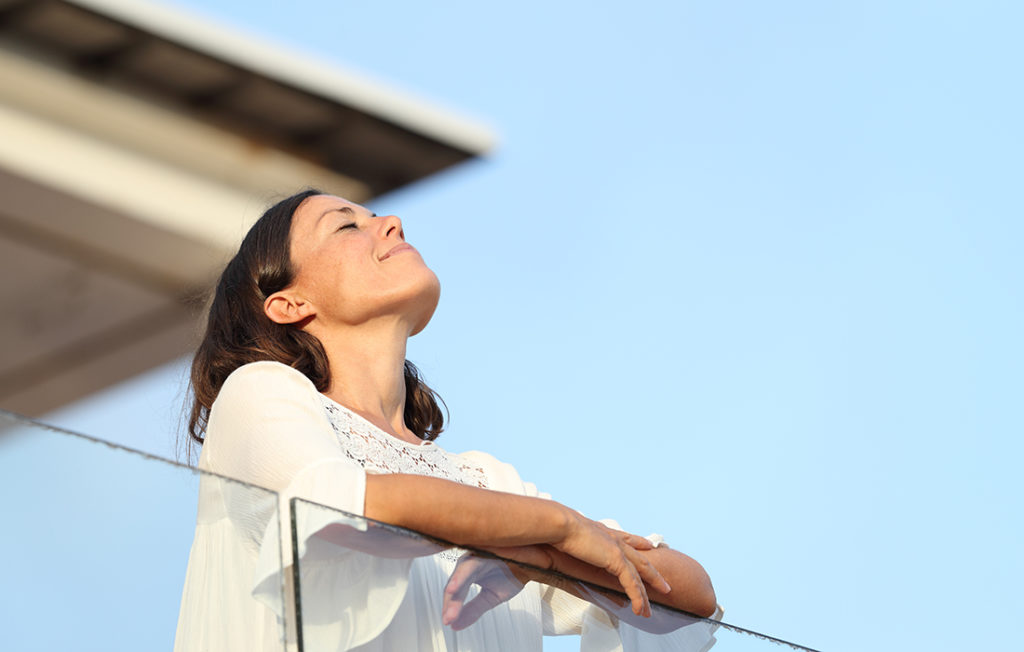 Relaxed adult woman breathing fresh air standing on a hotel balcony at summer; 