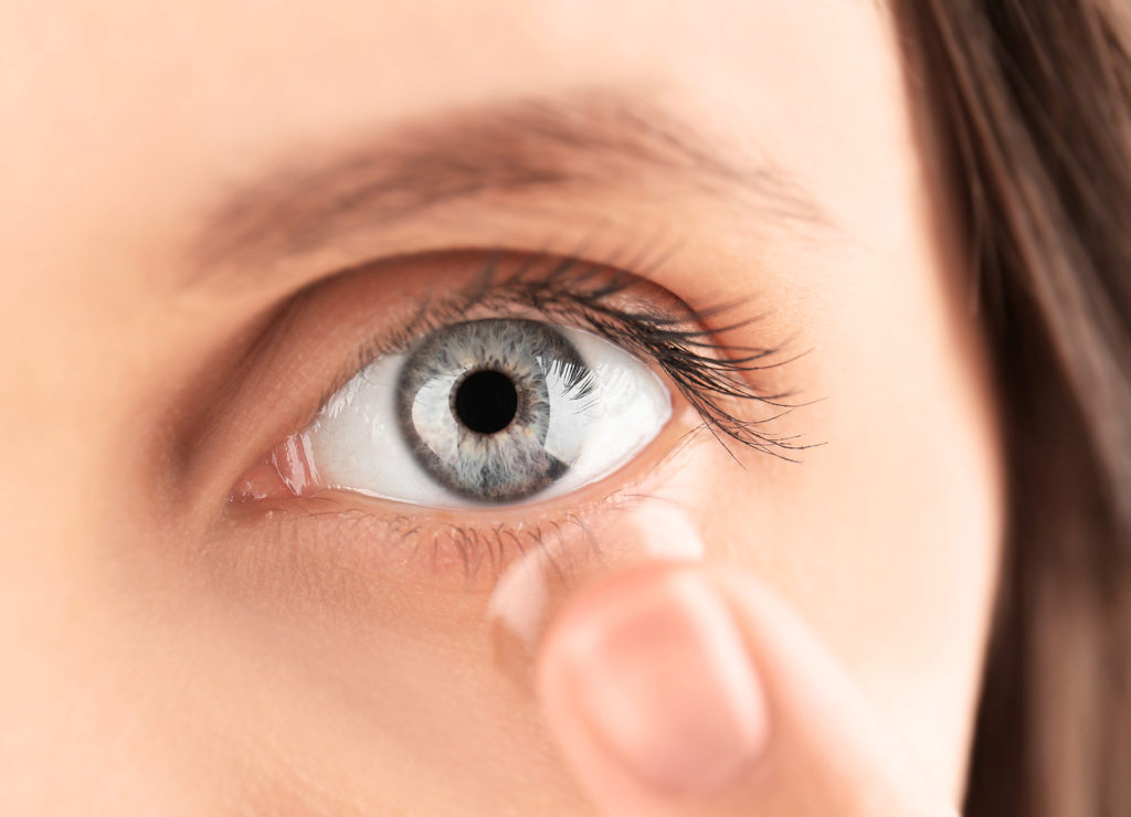 Close up view of young woman putting contact lens in her eye; 