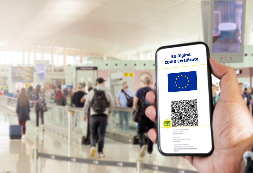 EU Digital COVID Certificate with the QR code on the screen of a mobile held by a hand with blurred airport in the background. Immunity from Covid-19. Travel without restrictions