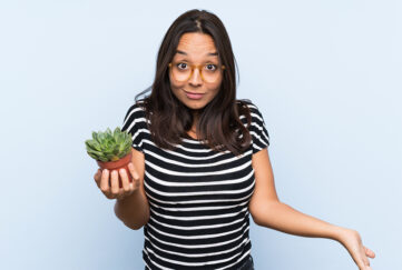 Young brunette woman holding a plant with shocked facial expression; ne