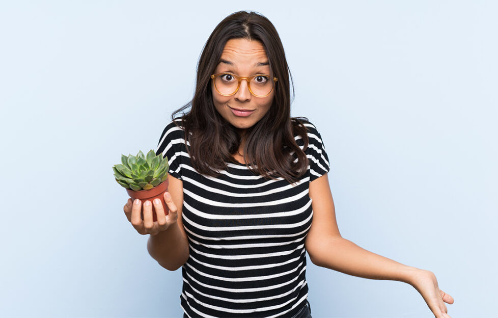 Young brunette woman holding a plant with shocked facial expression; ne