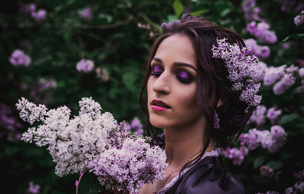 Lady in black and purple baroque dress smelling lilac blossom at dusk