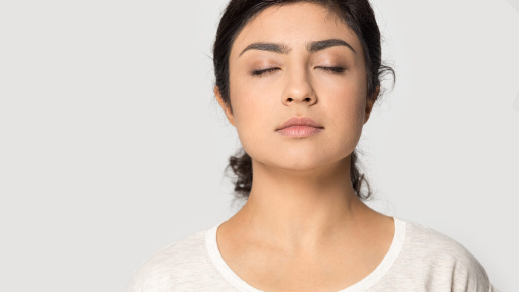Close up head shot cropped portrait young indian ethnicity mindful calm girl with closed eyes breathing fresh air, relaxing, deeply meditating near free empty copy space isolated on grey background.; 