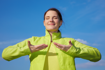 Brunette in lime green jacket doing breathing exercises outdoors