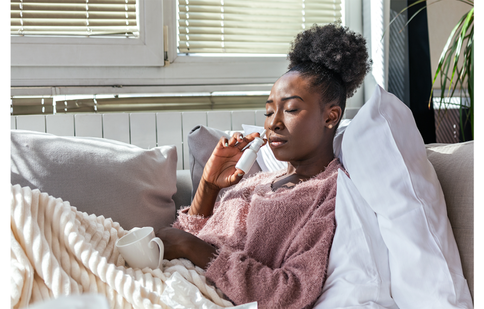 Black lady in bed ill with cup of tea and using nasal spray