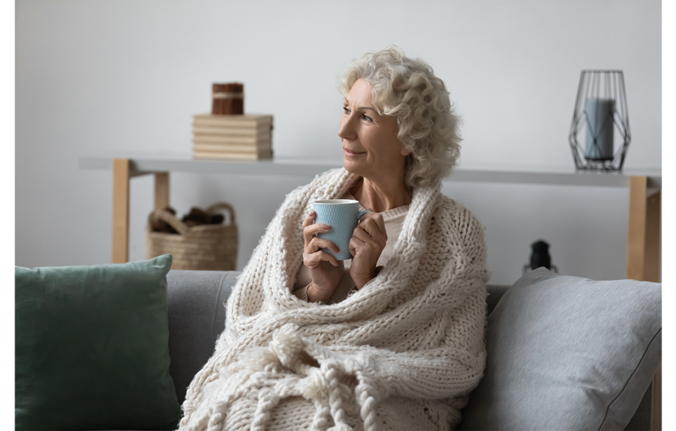 Older woman with blanket around her and cup of coffee sitting on settee