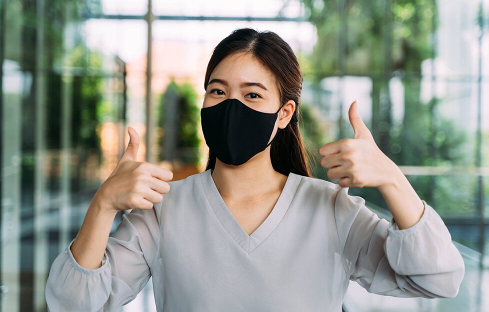 woman in mask gives thumbs up