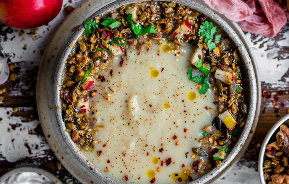 Bowl of neutral coloured soup with colourful savoury granola sprinkled around the edge in a crescent shape
