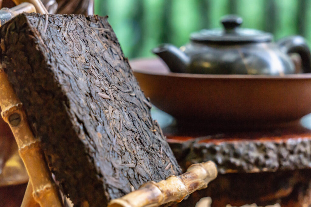 Puerh tea drinking in a traditional style on a wooden table. Antique tea-ware and figurines near tea bricks.; 