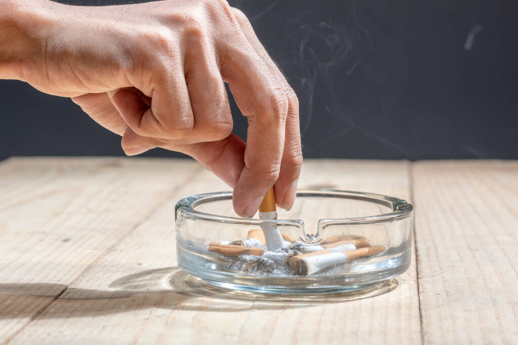 Hand stubbed out cigarette in a transparent ashtray on wooden table;