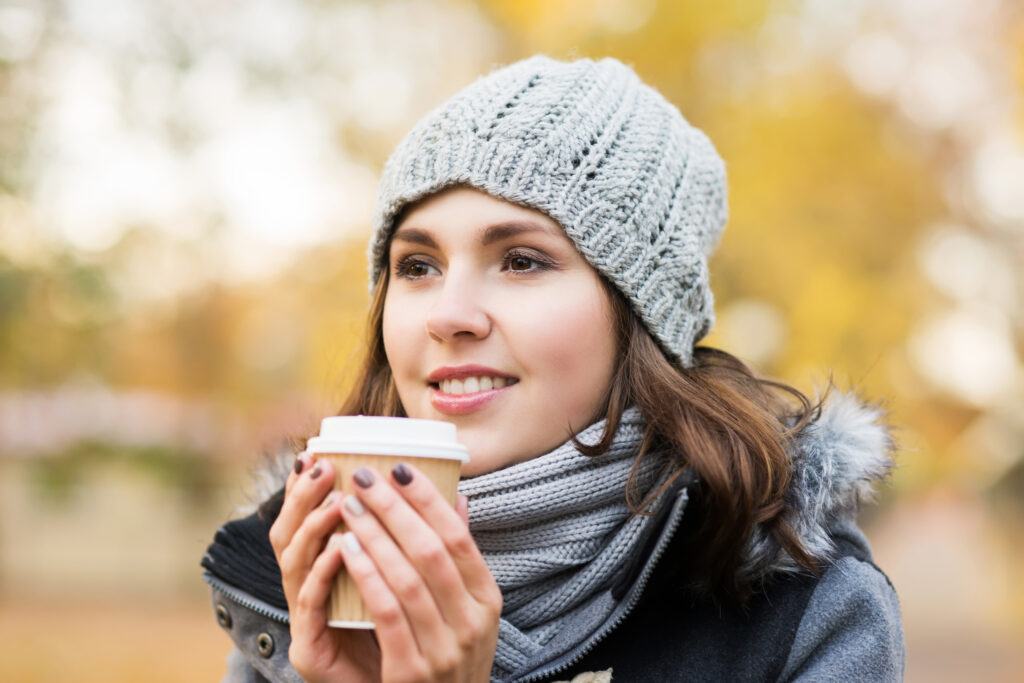 Young and beautiful girl drinking coffee in bright and colorful autumn park; 