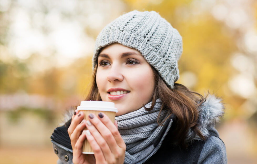 Young and beautiful girl drinking coffee in bright and colorful autumn park;