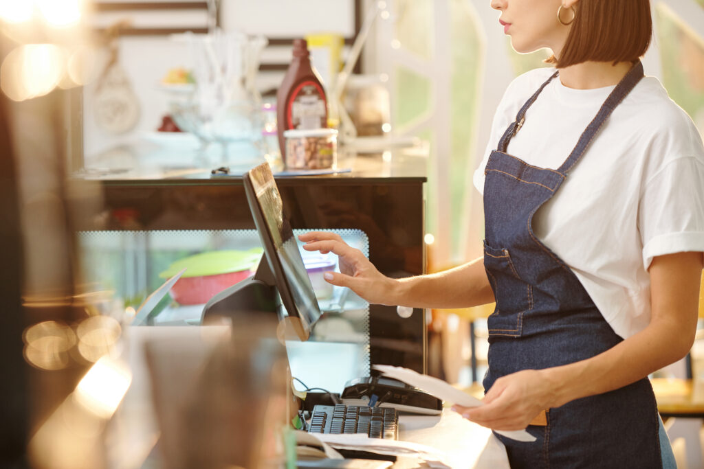 Cropped image of female barista working at coffeeshop and using cash register when accepting payment or entering order details