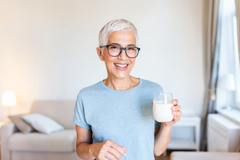 Portrait of a senior woman with a glass of milk. Beautiful elderly woman in grey T-shirt with a glass of milk. Senior woman drinking milk at home