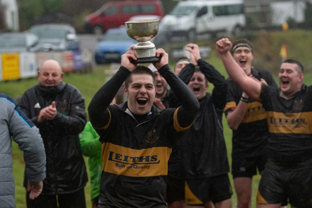 Lochaber captain Callum MacDonald lifts the trophy amid scenes of jubilation at a wet but happy Banavie on Saturday. NO F50 LRFC win bowl 03